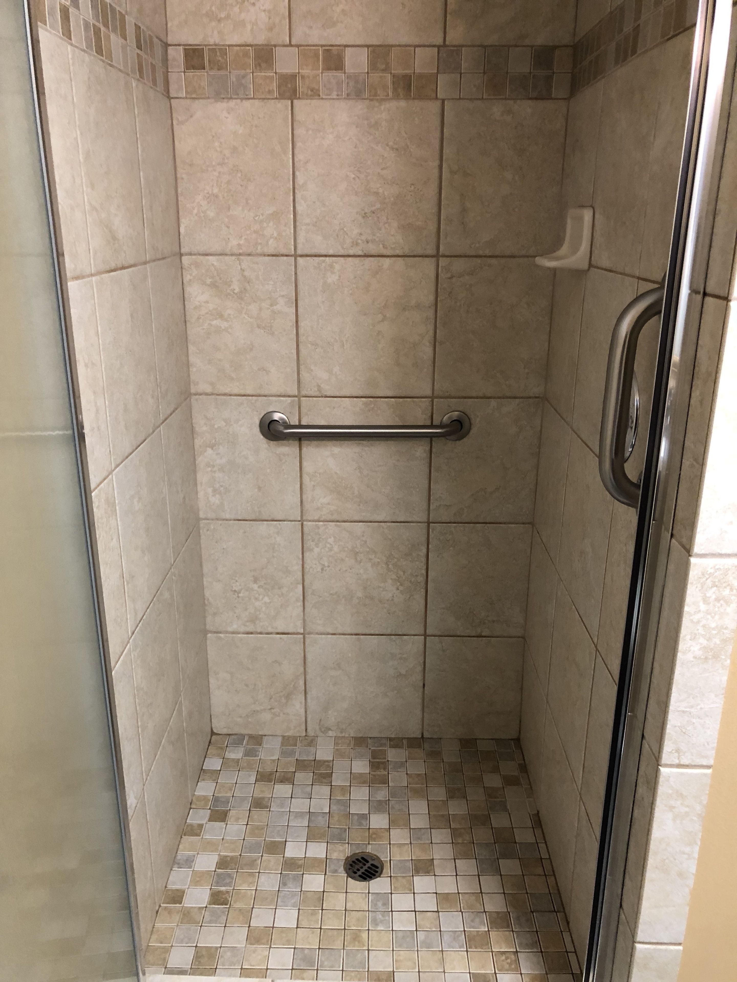 Une petite cabine de douche carrelée, équipée d’une barre d’appui et d’un drain.