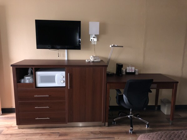 A wooden desk with a built-in microwave, a flat-screen TV mounted above it, and a lamp on the desk.