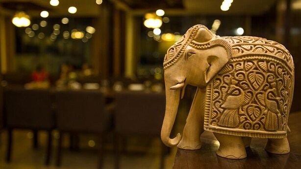 A carved elephant statue in a warmly lit room with tables and chairs. - Mahadev Hotel (Kathmandu)