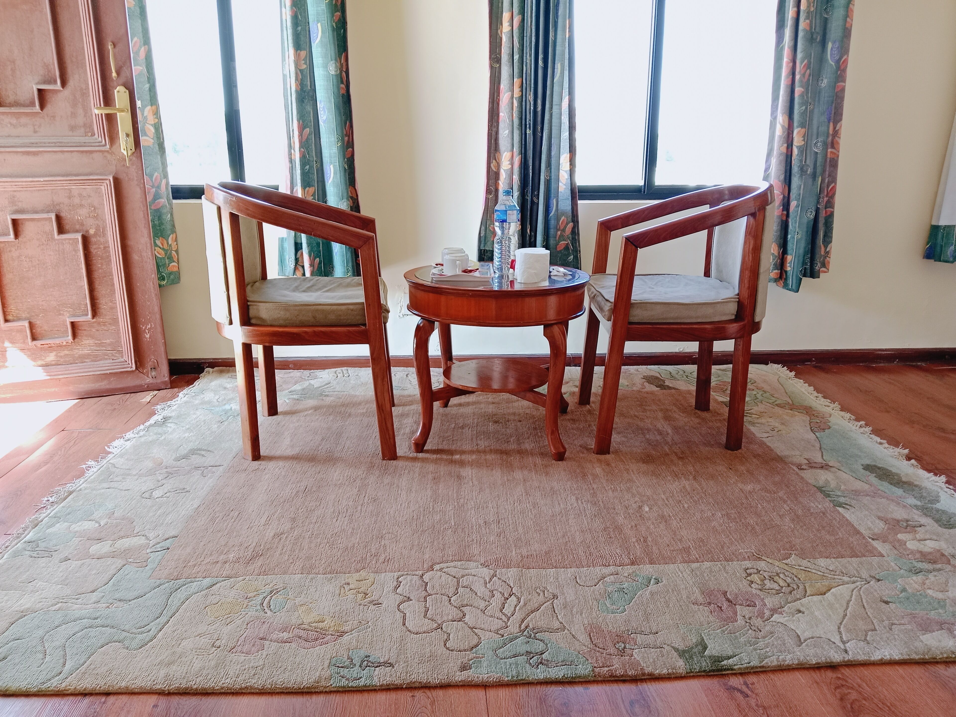 Une pièce avec deux chaises en bois et une petite table ronde, un tapis à motifs floraux et un plancher en bois.