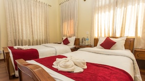 A hotel room with two beds, each with a red blanket and white pillows. There is a wooden headboard on the left bed, and a small table with a kettle and a bottle of water on the right. - Hotel Norbu Sangpo (Kathmandu)
