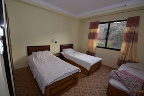 A room with two single beds, a small table, a wall-mounted lamp, and a window with curtains. - Kirtipur Hillside Hotel and Resort (Kirtipur)