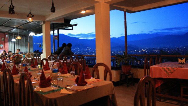 Ein Restaurant mit gedeckten Tischen, Blick auf die Stadt und Berge im Hintergrund.