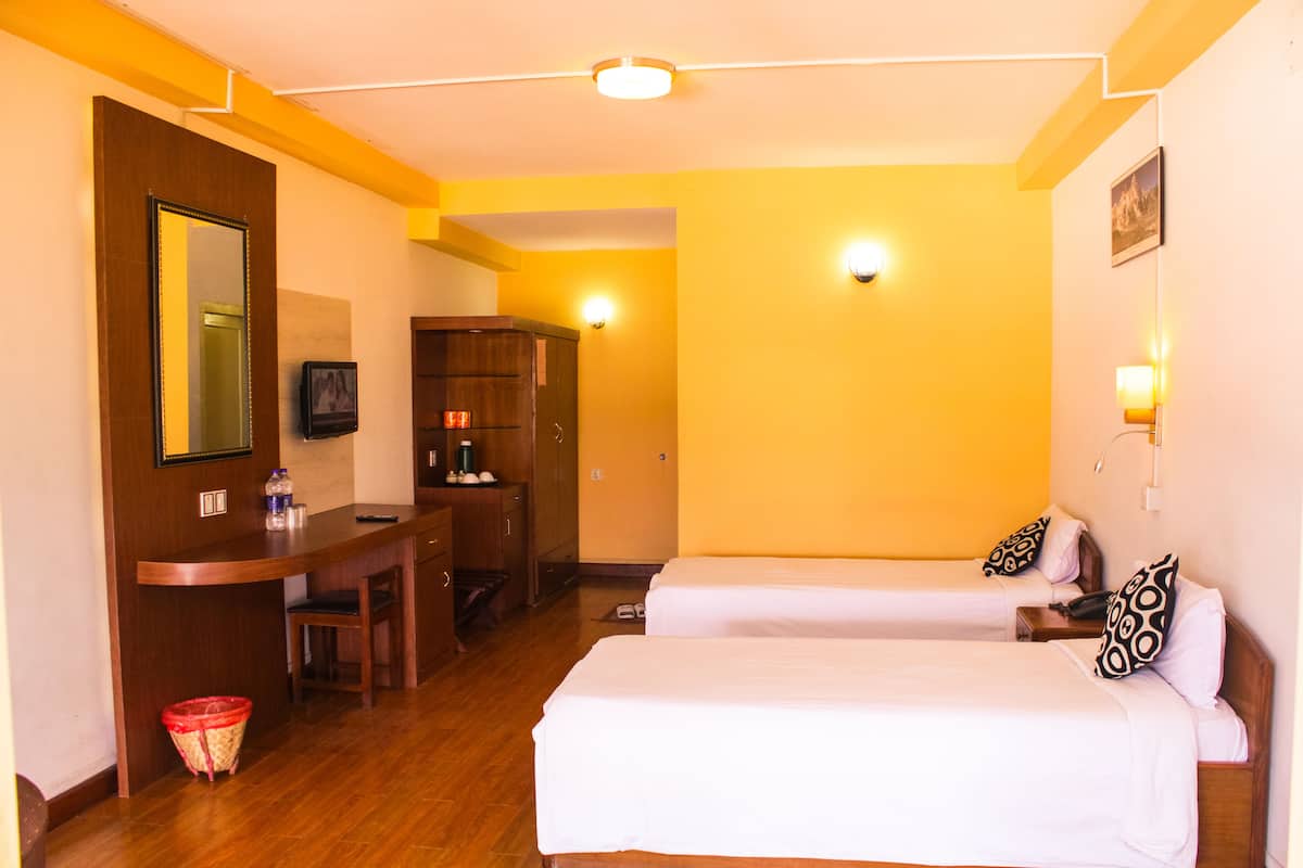 A hotel room with two beds, a desk, a chair, a wooden wardrobe, and a mirror.