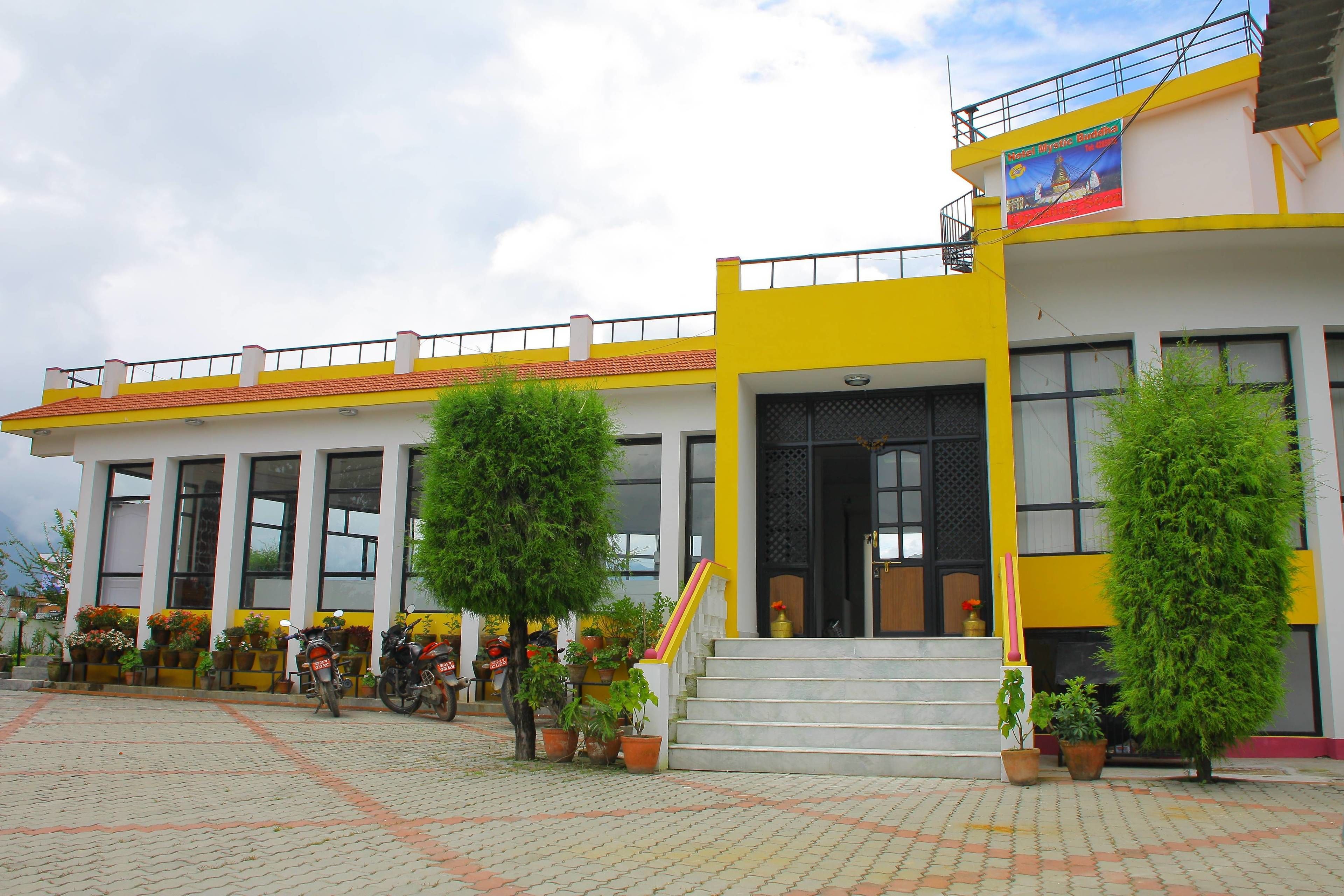 A building with a yellow and white facade, large windows, and a staircase leading to the entrance.