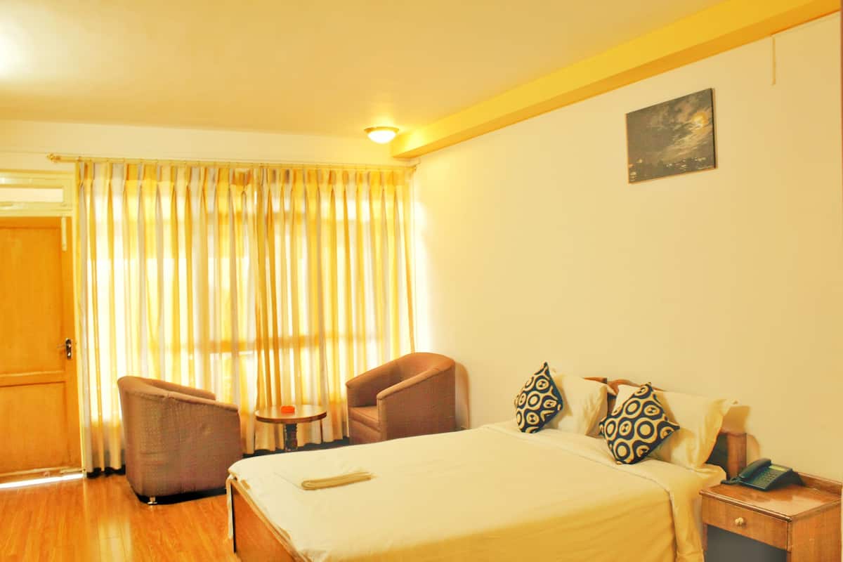 A hotel room with a bed, two chairs, a bedside table with a phone, and a curtain.