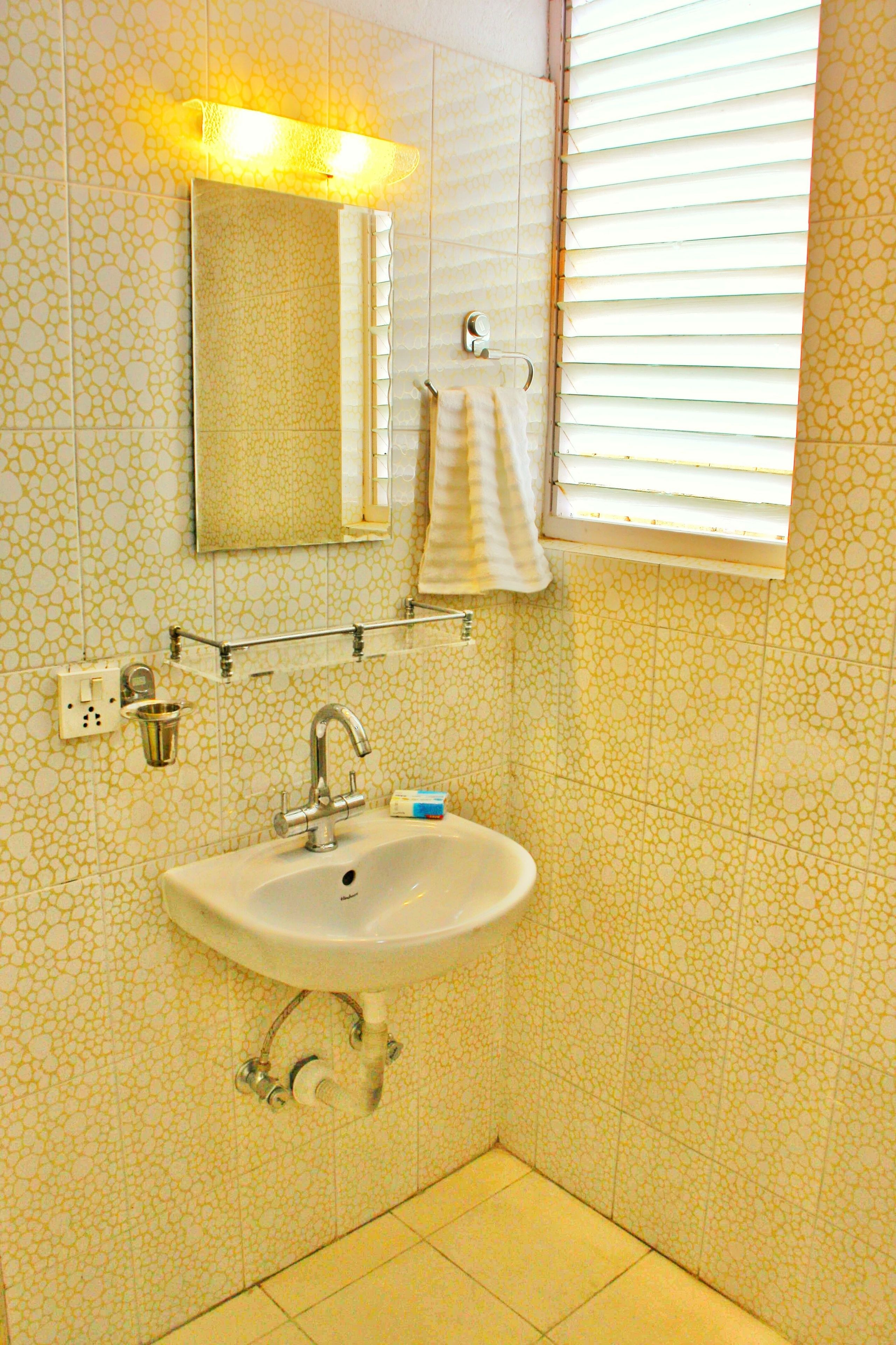 Un baño con lavamanos, espejo y ventana con persianas.