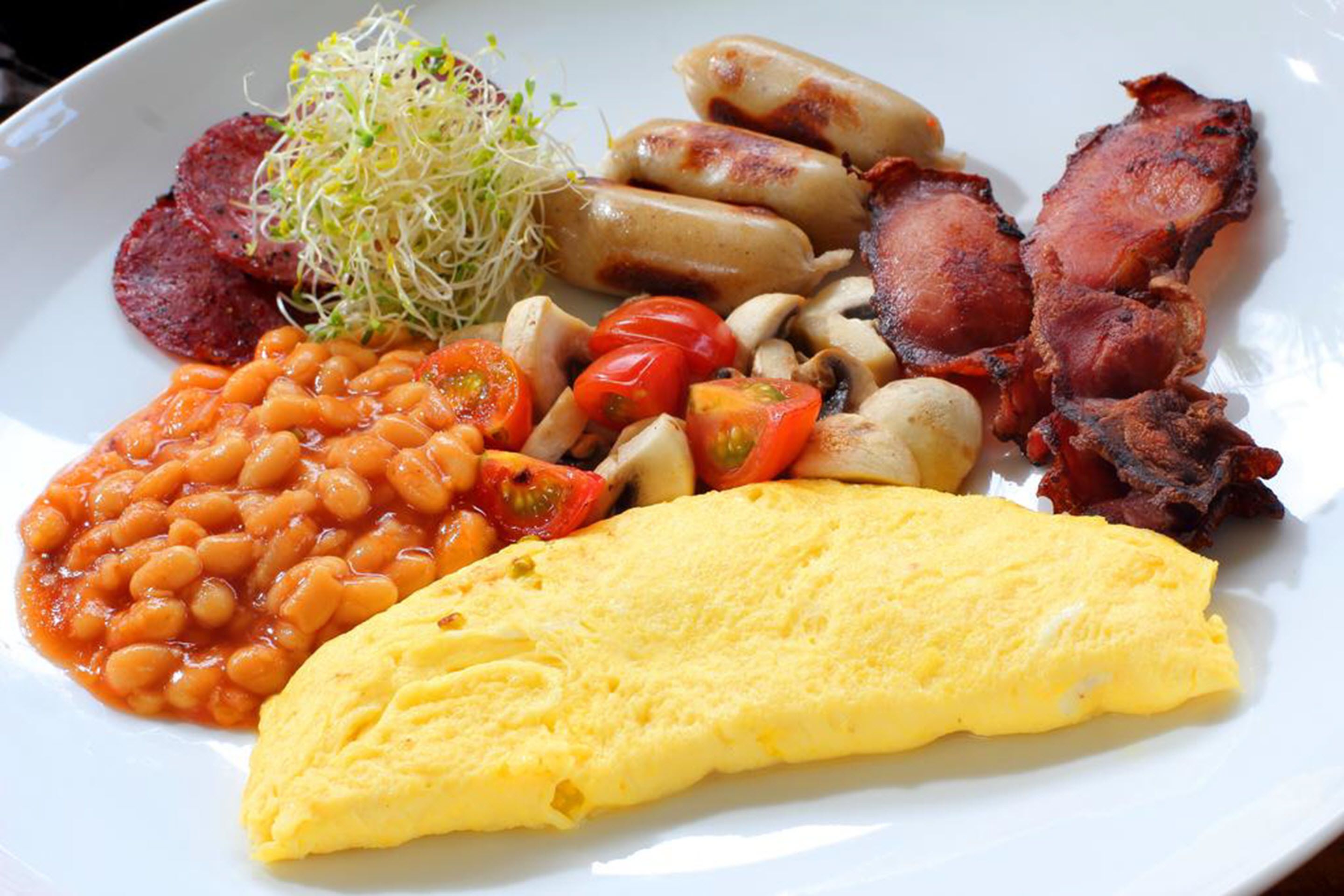 Un plato con frijoles, tomates, champiñones, tocino, salchichas y una tortilla.