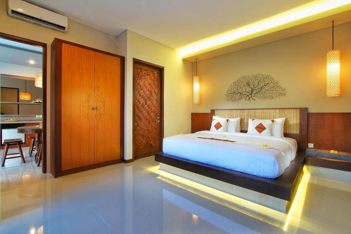 Une chambre d’hôtel moderne dotée d’un grand lit, d’une armoire en bois, d’un coin repas et d’un luminaire fixé au mur.