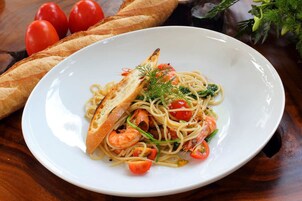 A plate of spaghetti with shrimp, tomatoes, and herbs, accompanied by slices of toasted bread.