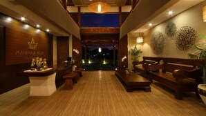 Vestíbulo de hotel con suelo de madera, mostrador de recepción, bancos e iluminación decorativa en las paredes.