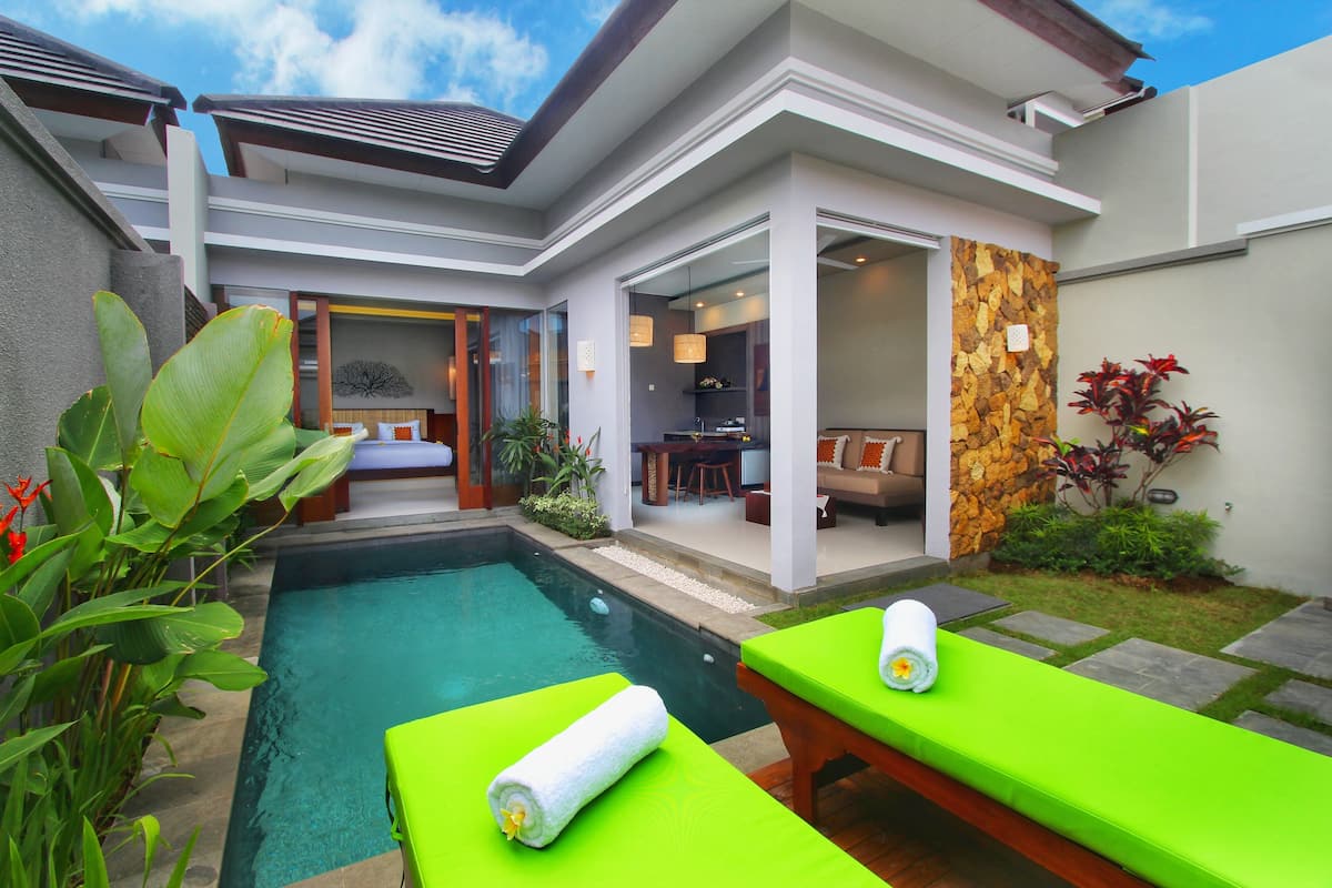 Una casa moderna con piscina, sillas de descanso verdes y un jardín bien cuidado.