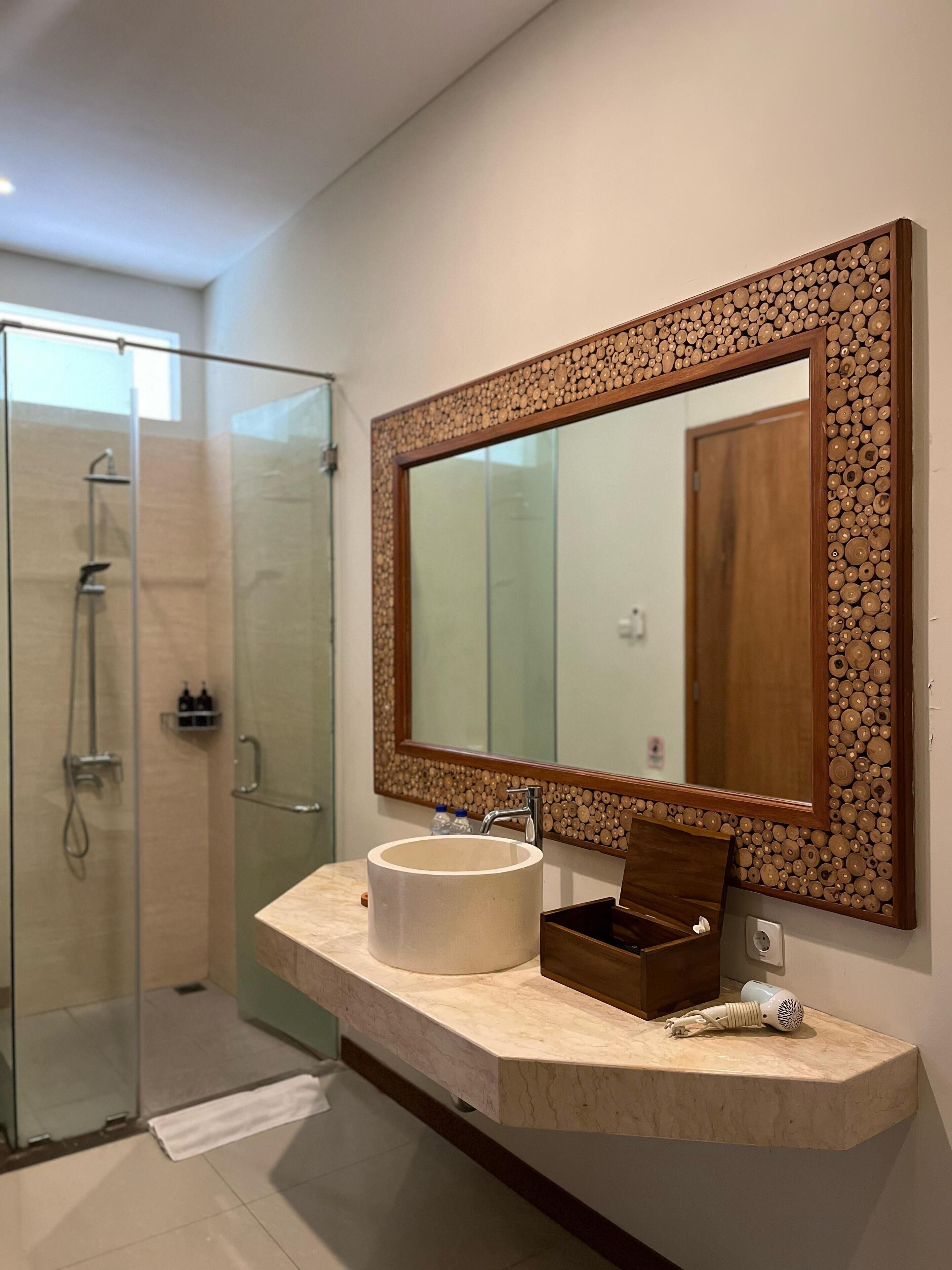 A bathroom with a glass shower enclosure, a large mirror with a wooden frame, a marble sink, and a towel rack.