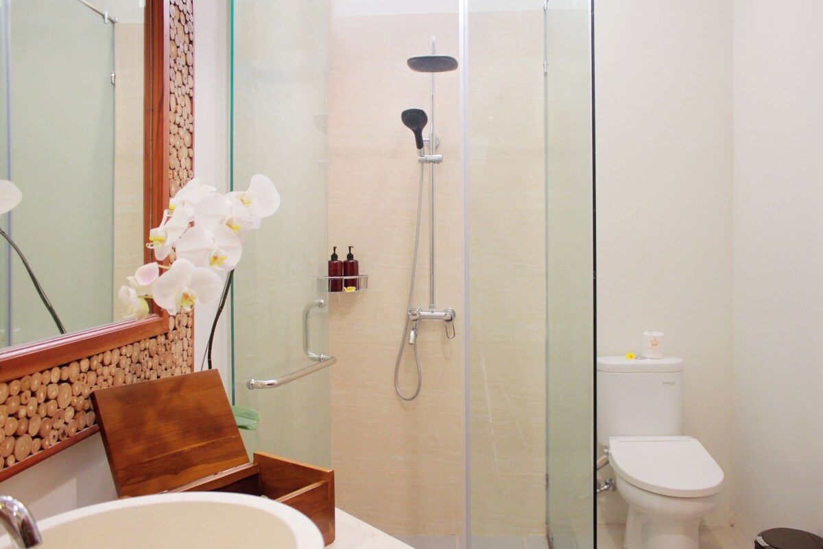 A bathroom with a glass shower enclosure, a toilet, and a sink with a mirror.