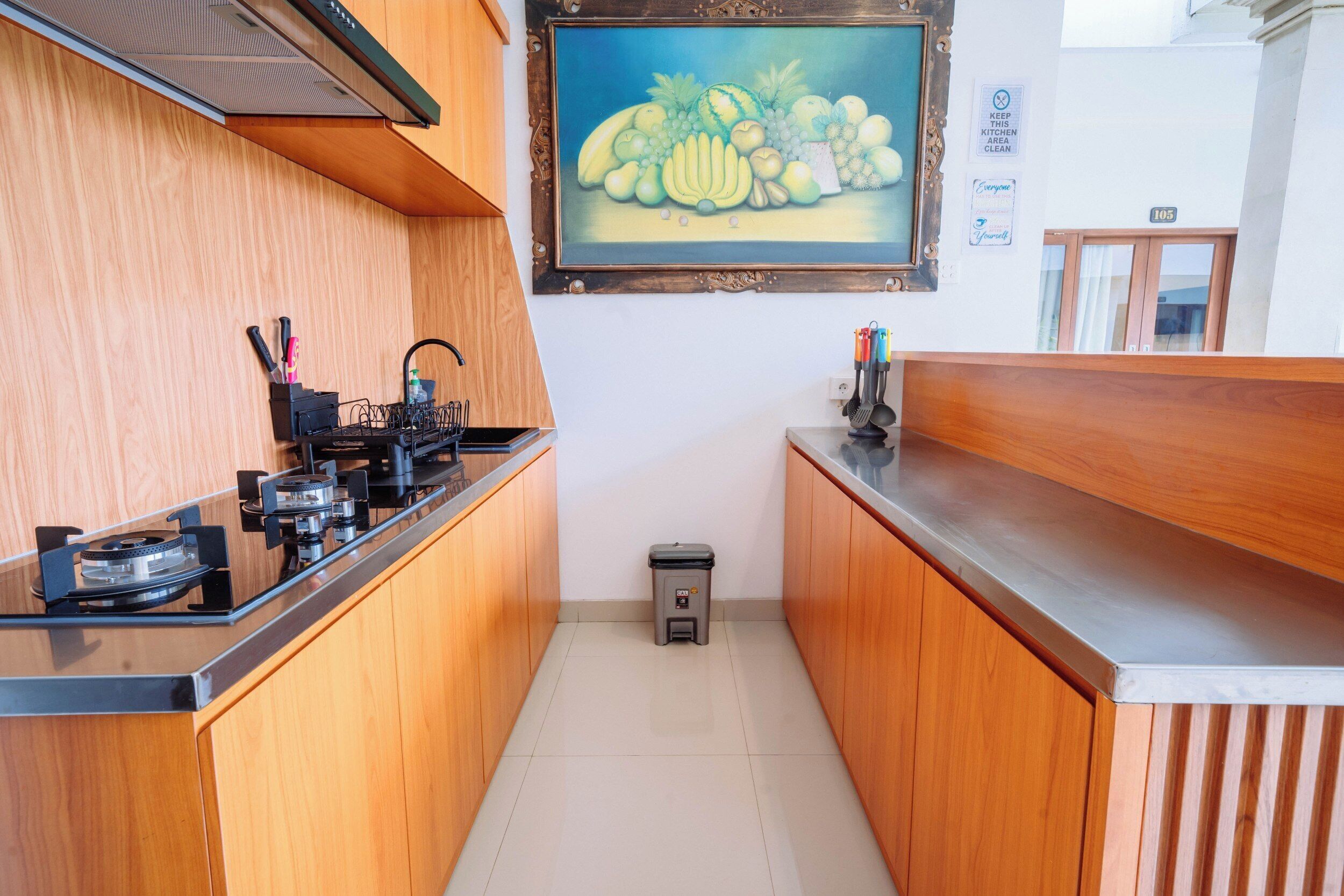 Une cuisine étroite avec des meubles de rangement en bois, une cuisinière à gaz et une poubelle.