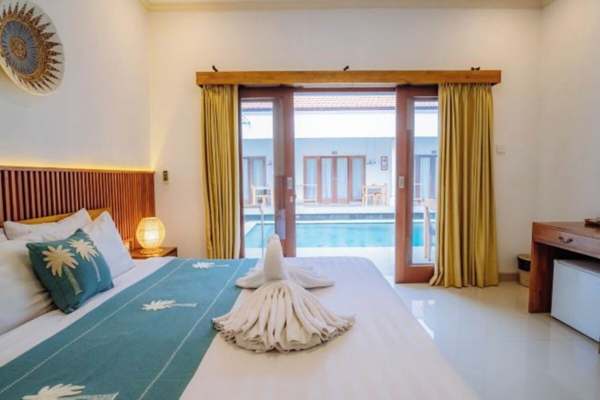 Habitación de hotel con cama, escritorio, lámpara y vistas a una piscina y un edificio.