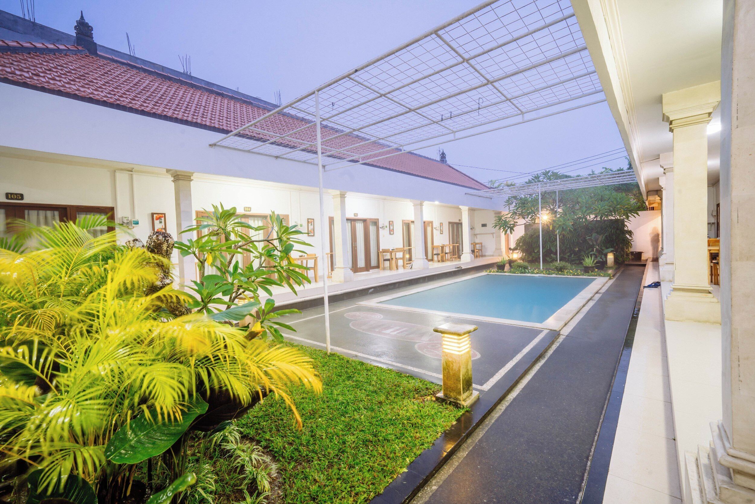 A hotel courtyard with a swimming pool, covered seating area, and lush greenery.