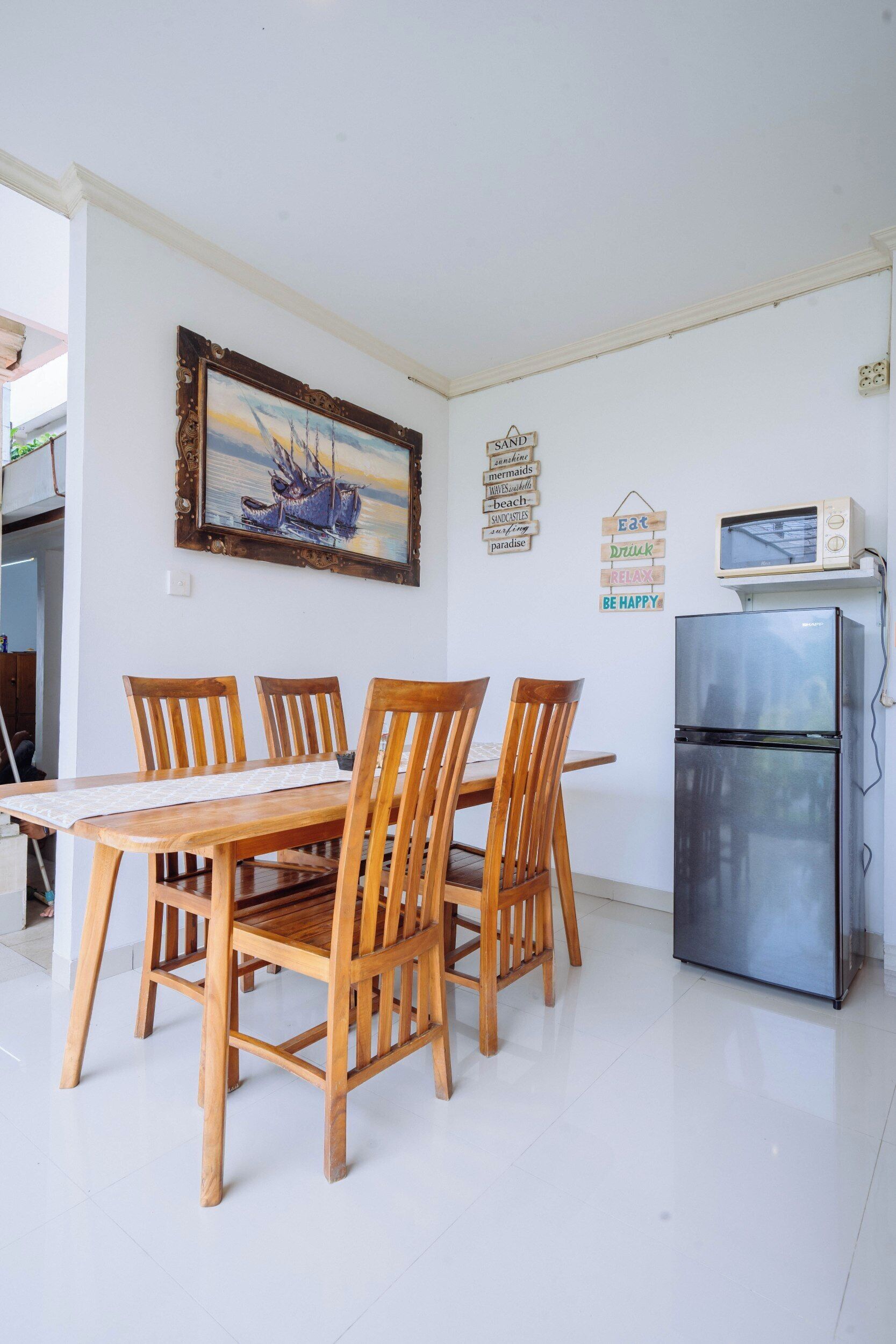 A dining area with a wooden table and chairs, a refrigerator, and a framed painting on the wall.