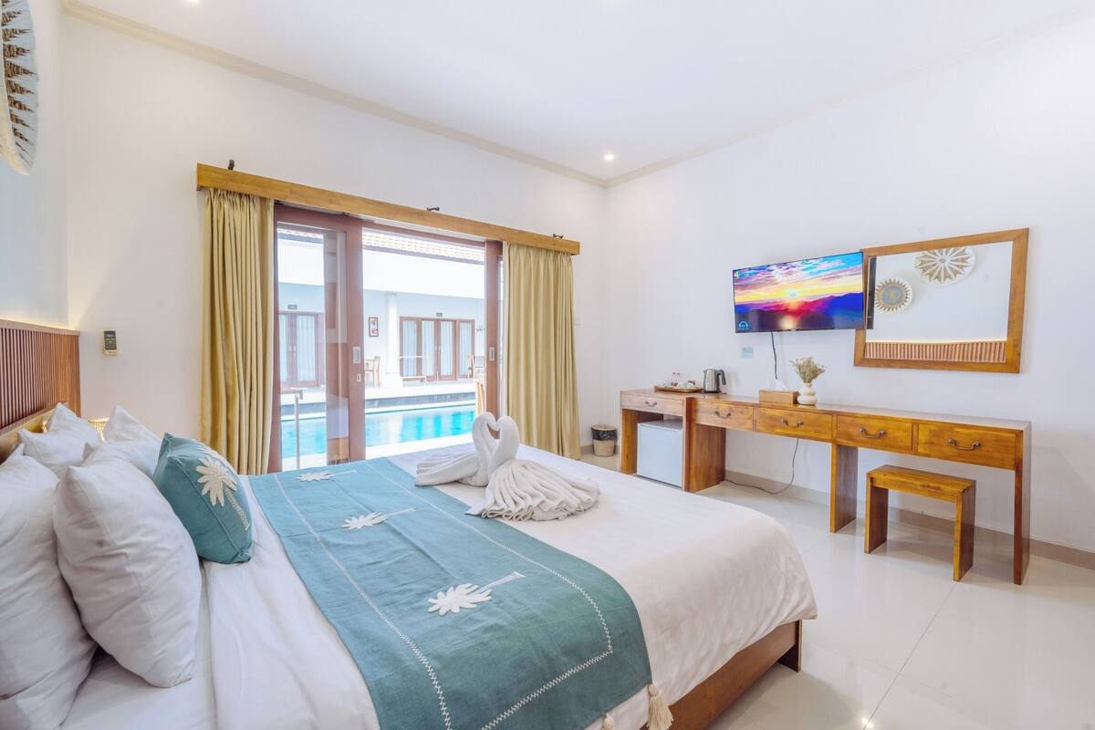 A hotel room with a bed, a desk, a TV, and a view of the pool.