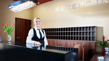 Un mostrador de recepción con una recepcionista, una araña de cristal, un letrero en la pared que dice "RECEPTION" y un gabinete de madera con divisiones.