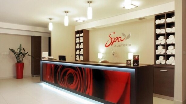 Un área de recepción de diseño moderno, con un mostrador central que presenta un diseño abstracto rojo, un letrero que dice "Spa Austria" y estantes con toallas dobladas.