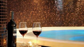 A bottle of wine and two glasses on a table next to a hot tub with a tiled wall in the background.