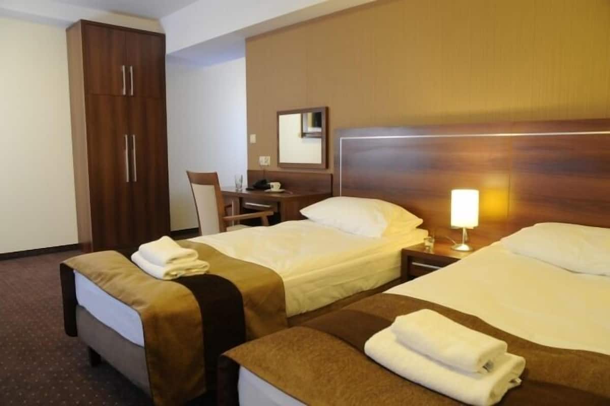 A hotel room with two beds, a desk, a chair, a wardrobe, and a bedside lamp.