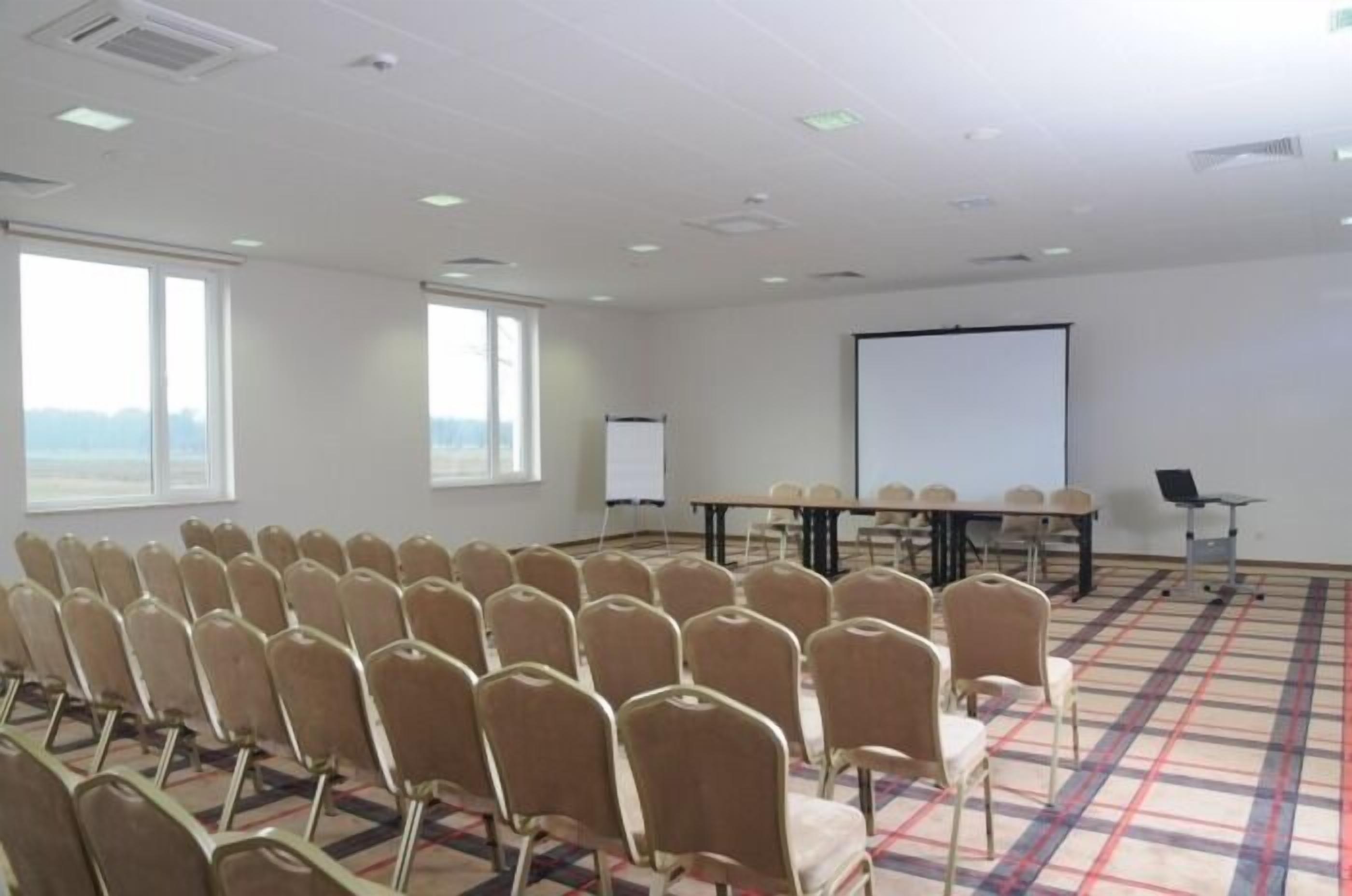 A conference room with rows of chairs, a large table, a projector screen, and a whiteboard.