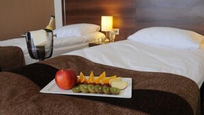 Una habitación de hotel con una cama, una mesita de noche con una botella de champán y un plato de fruta.