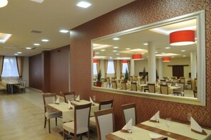 A dining area with tables and chairs, a large mirror reflecting the room, and a patterned wall. - Hotel Austeria Conference & Spa (Ciechocinek)