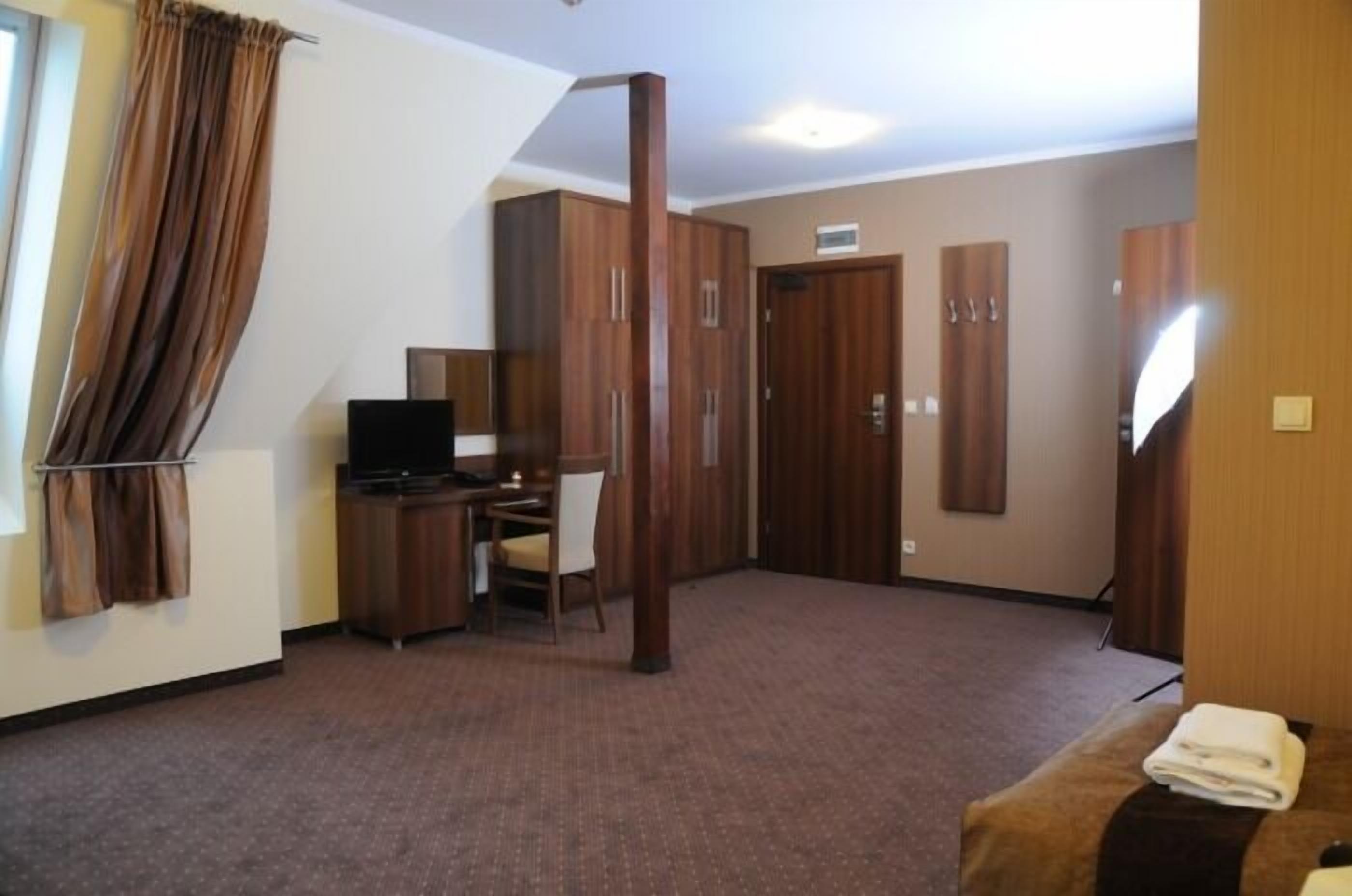 A hotel room with a desk, chair, wardrobe, and a bed.