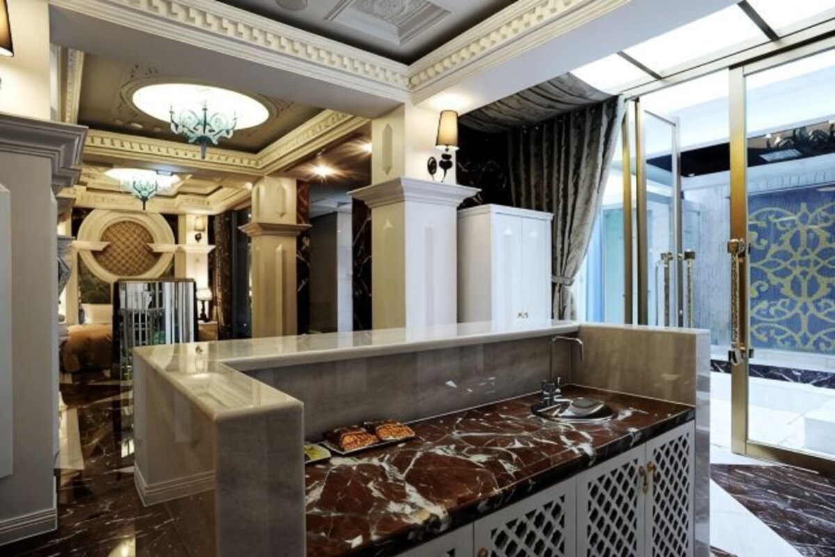 A lobby with a marble reception desk, a chandelier, and a patterned wall.
