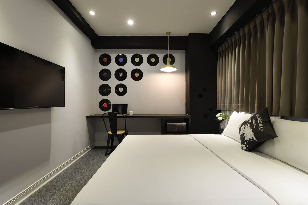 Quarto moderno com cama, escrivaninha, cadeira, TV fixada na parede e uma parede cheia de discos de vinil.