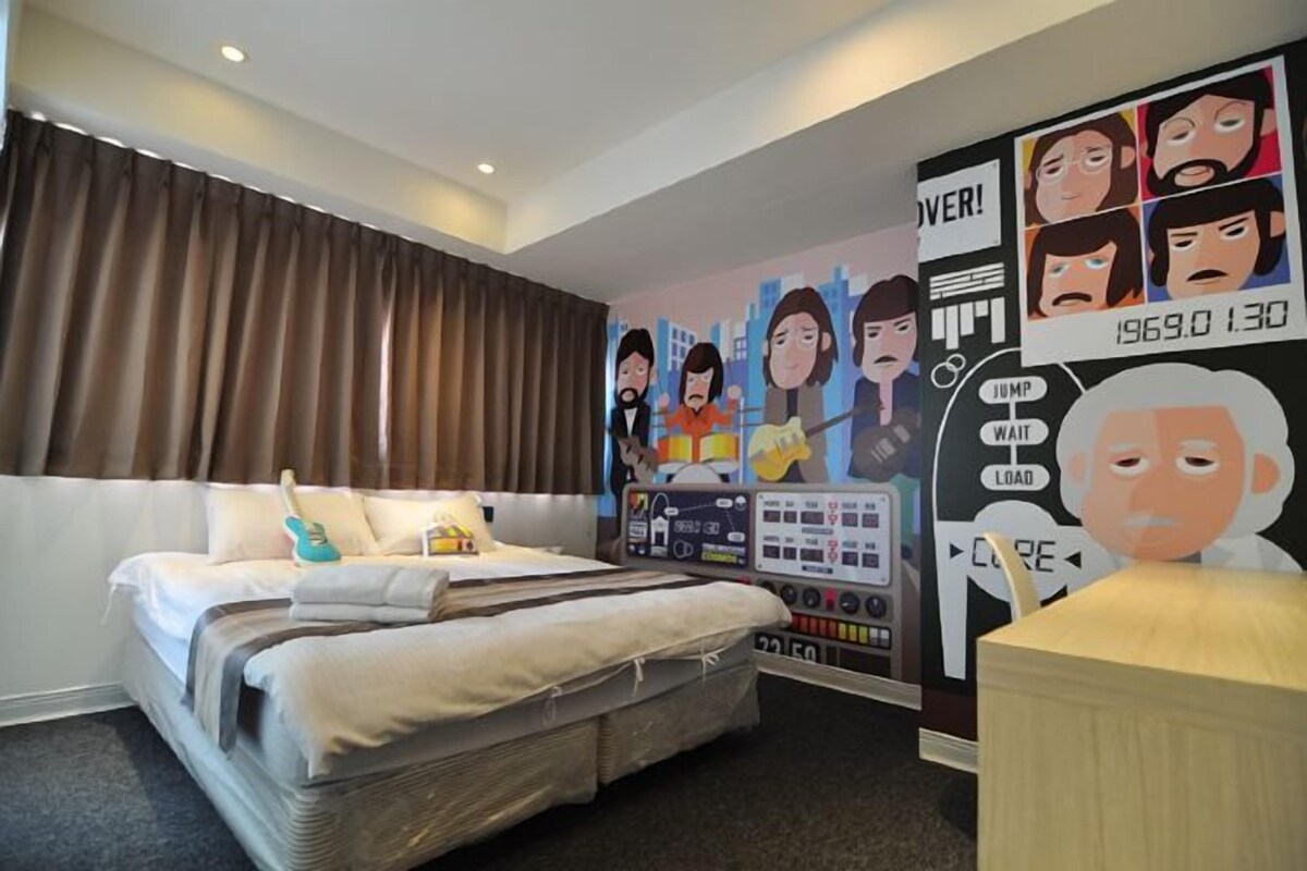 A hotel room with a bed, a desk, and a wall with cartoon characters.