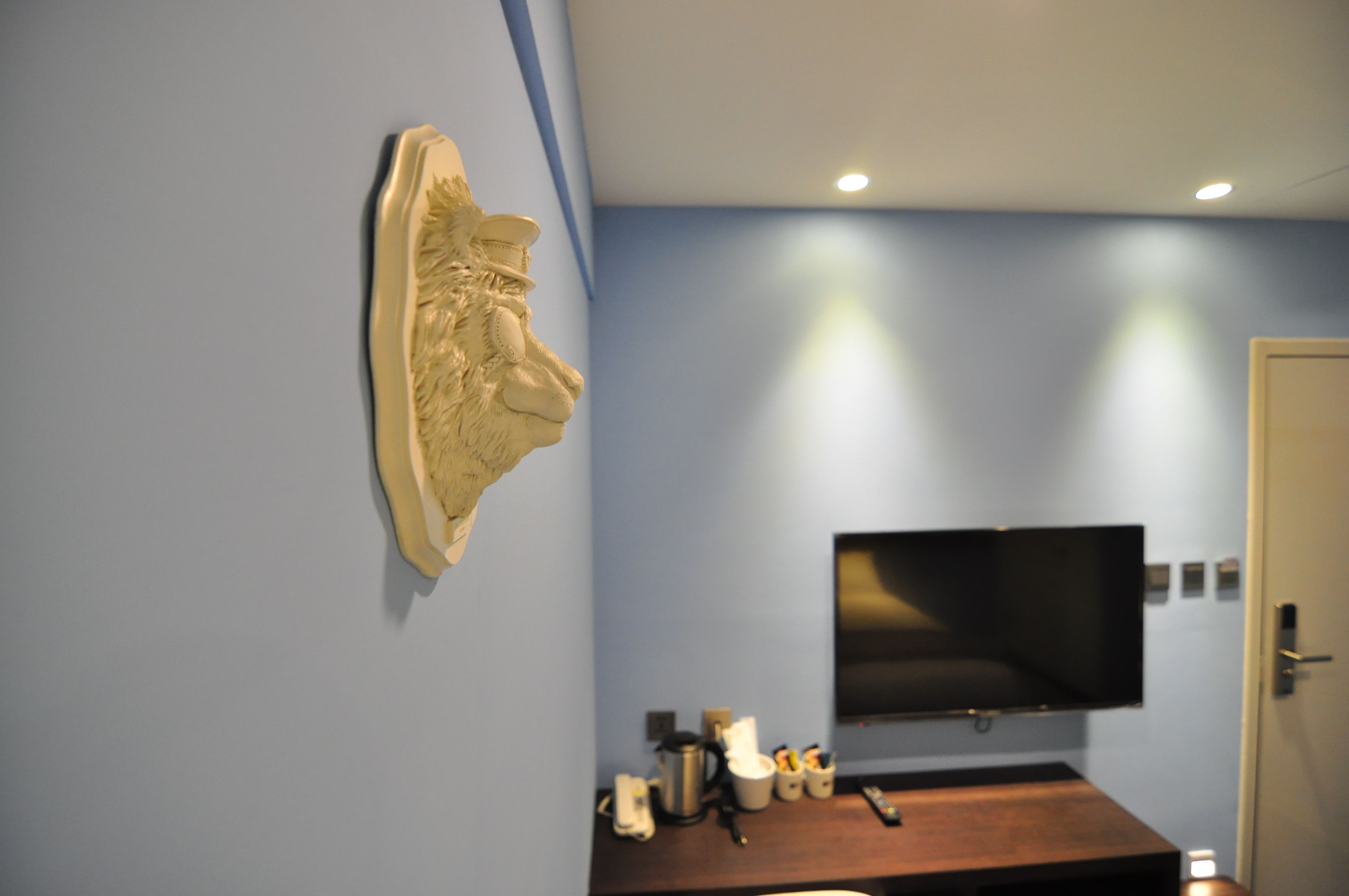 Une pièce dans laquelle on trouve une sculpture fixée au mur, un téléviseur à écran plat également fixé au mur, et une table en bois sur laquelle sont disposés divers objets.