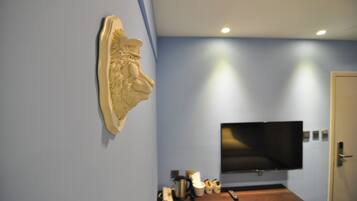 Une pièce dans laquelle on trouve une sculpture fixée au mur, un téléviseur à écran plat également fixé au mur, et une table en bois sur laquelle sont disposés divers objets.