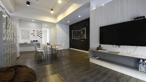 A modern hotel room with a wooden floor, a dining area with a table and chairs, a large TV mounted on the wall, and a minibar. - Taichung Box Design Hotel (Taichung)
