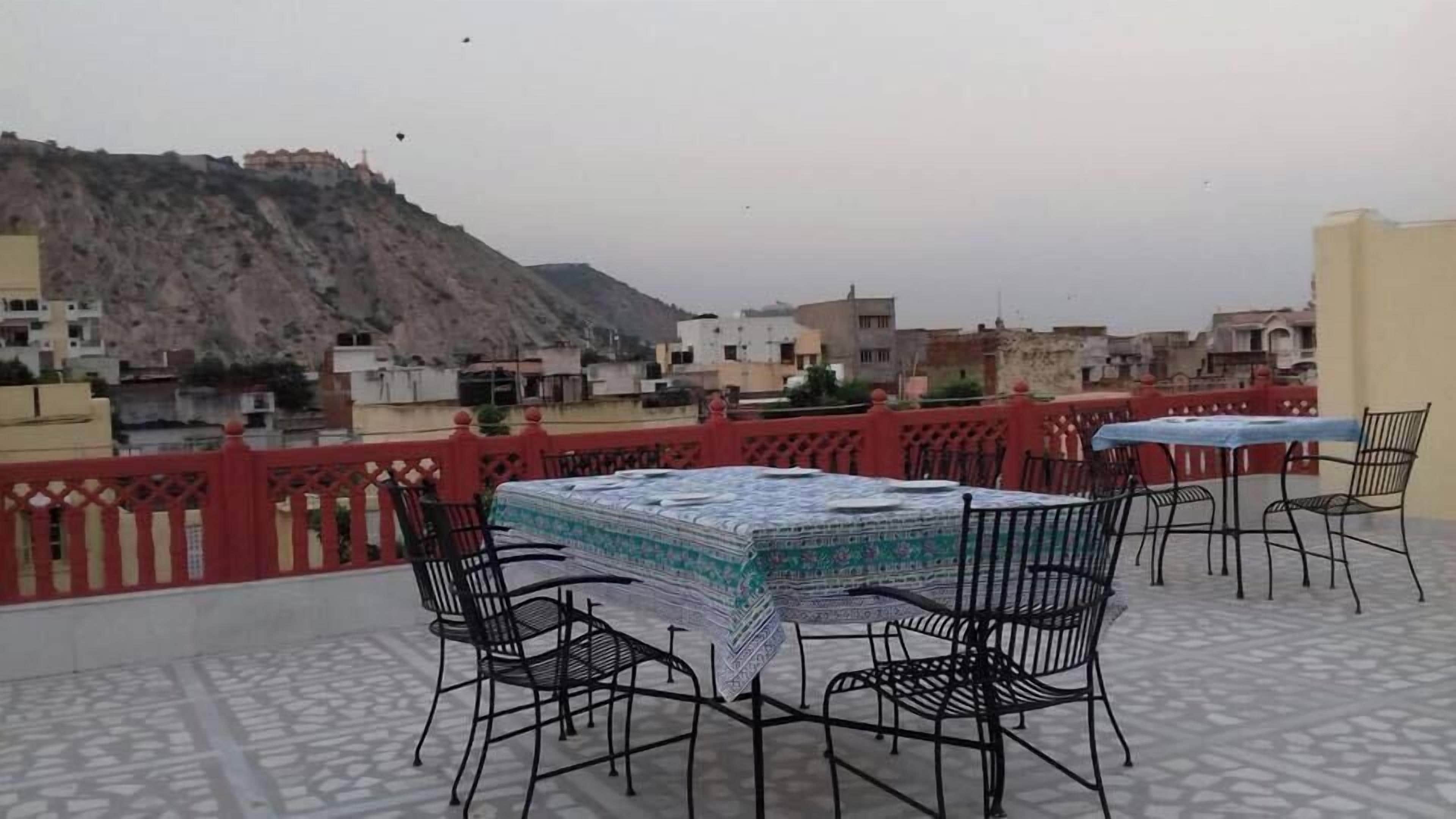 Terraza exterior con mantel estampado, sillas de metal y barandilla roja.