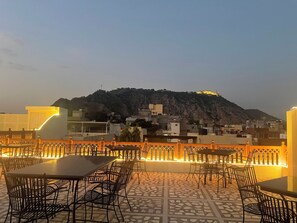 An outdoor seating area with tables and chairs, a patterned floor, and a view of a hill with buildings in the background. - Khatu Haveli (Jaipur)