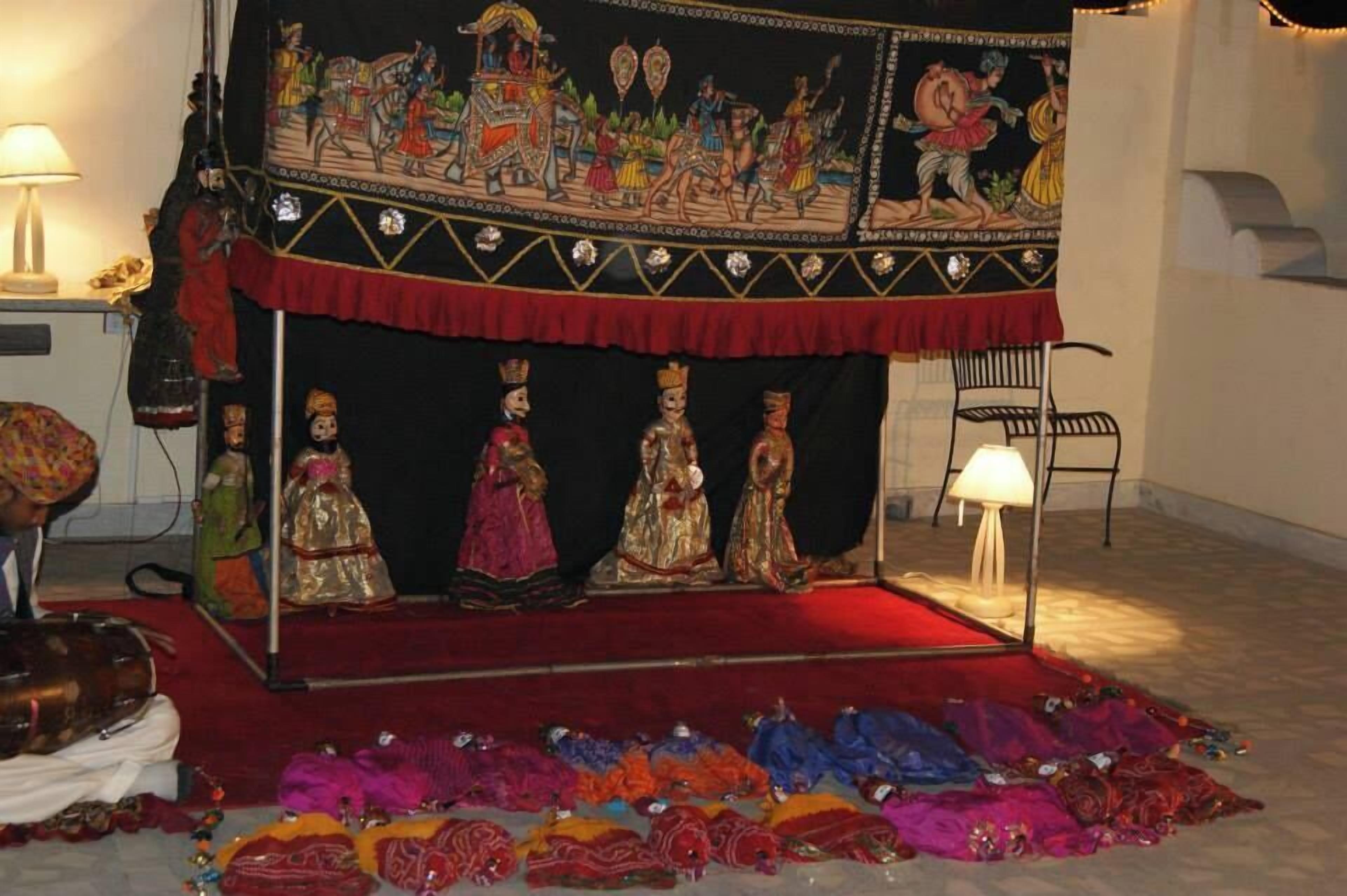 Una habitación con alfombra roja, un fondo negro con obras de arte coloridas y una fila de maniquíes vestidos con trajes tradicionales.