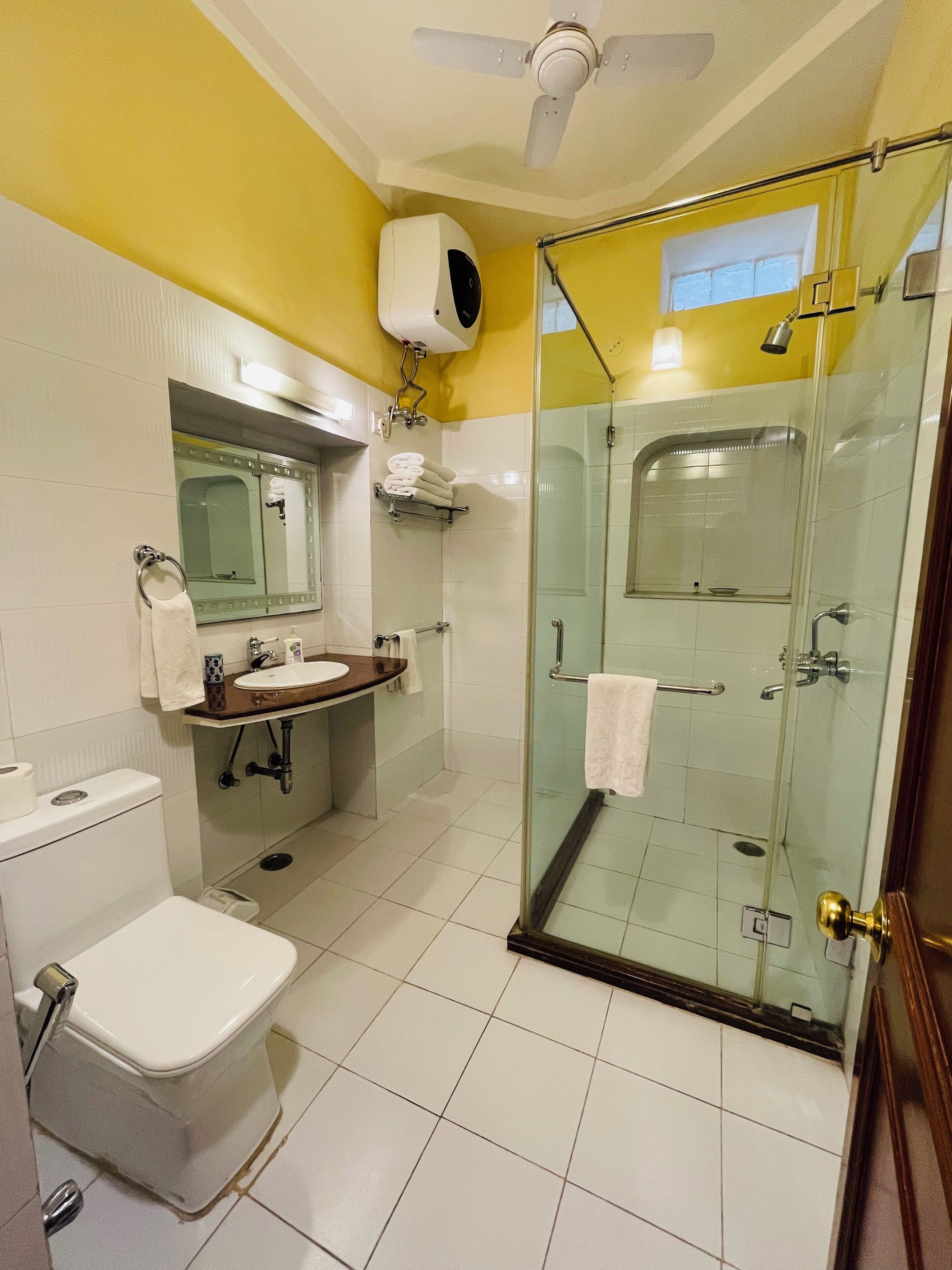 Un baño con inodoro, lavamanos, espejo y ducha con mampara de vidrio.