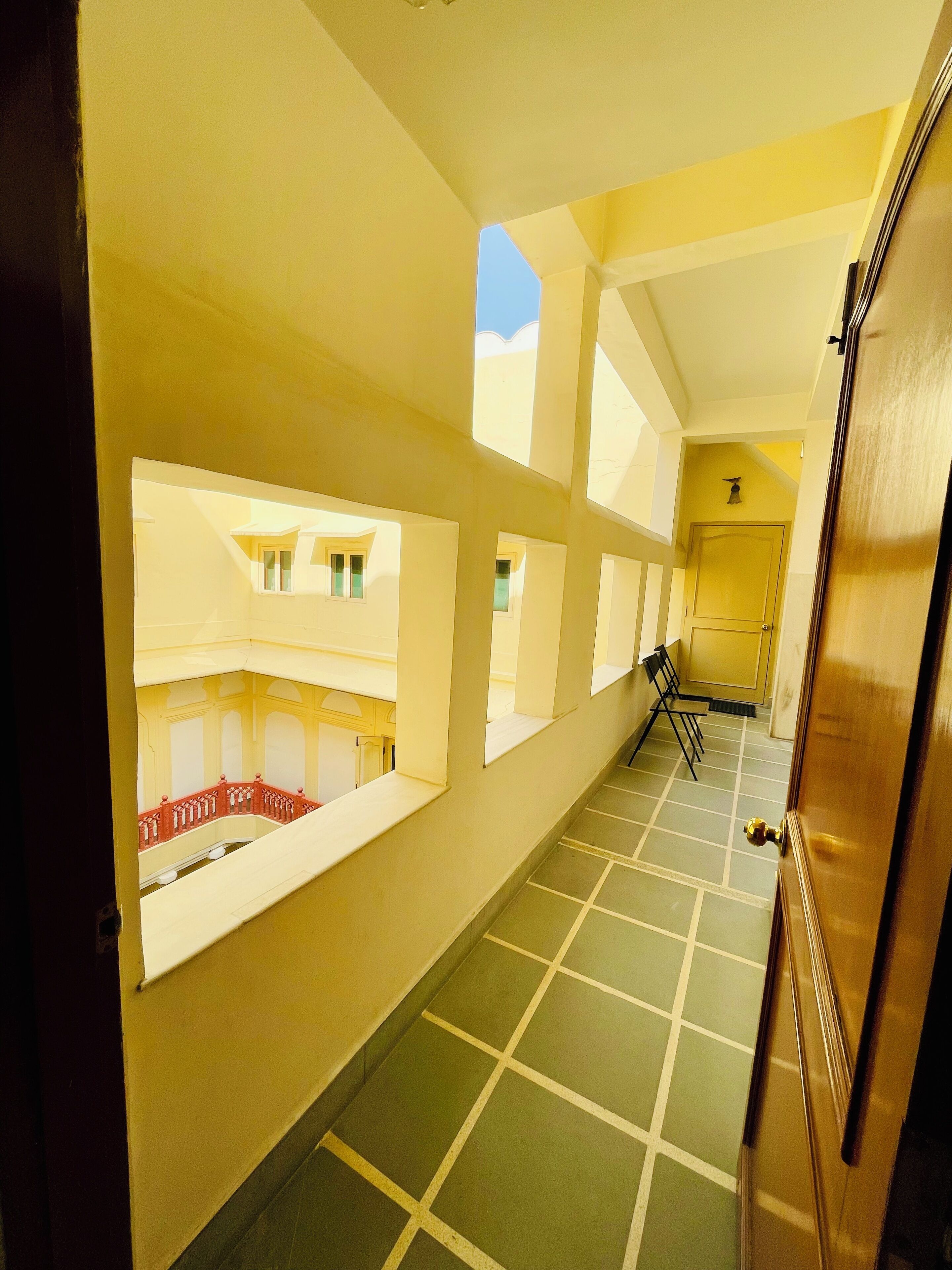Ein Korridor mit gefliestem Boden, einer Holztür und Blick auf einen Balkon mit Geländer.