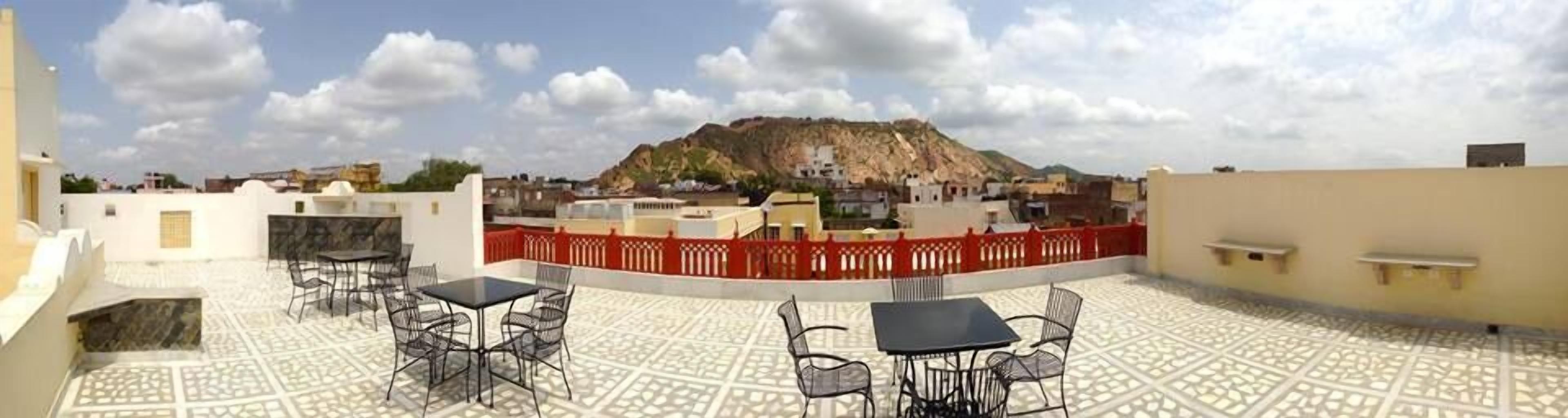 A rooftop terrace with tables and chairs, a red fence, and a view of a mountain.