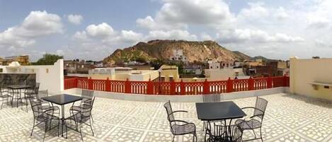 A rooftop terrace with tables and chairs, a red fence, and a view of a mountain.