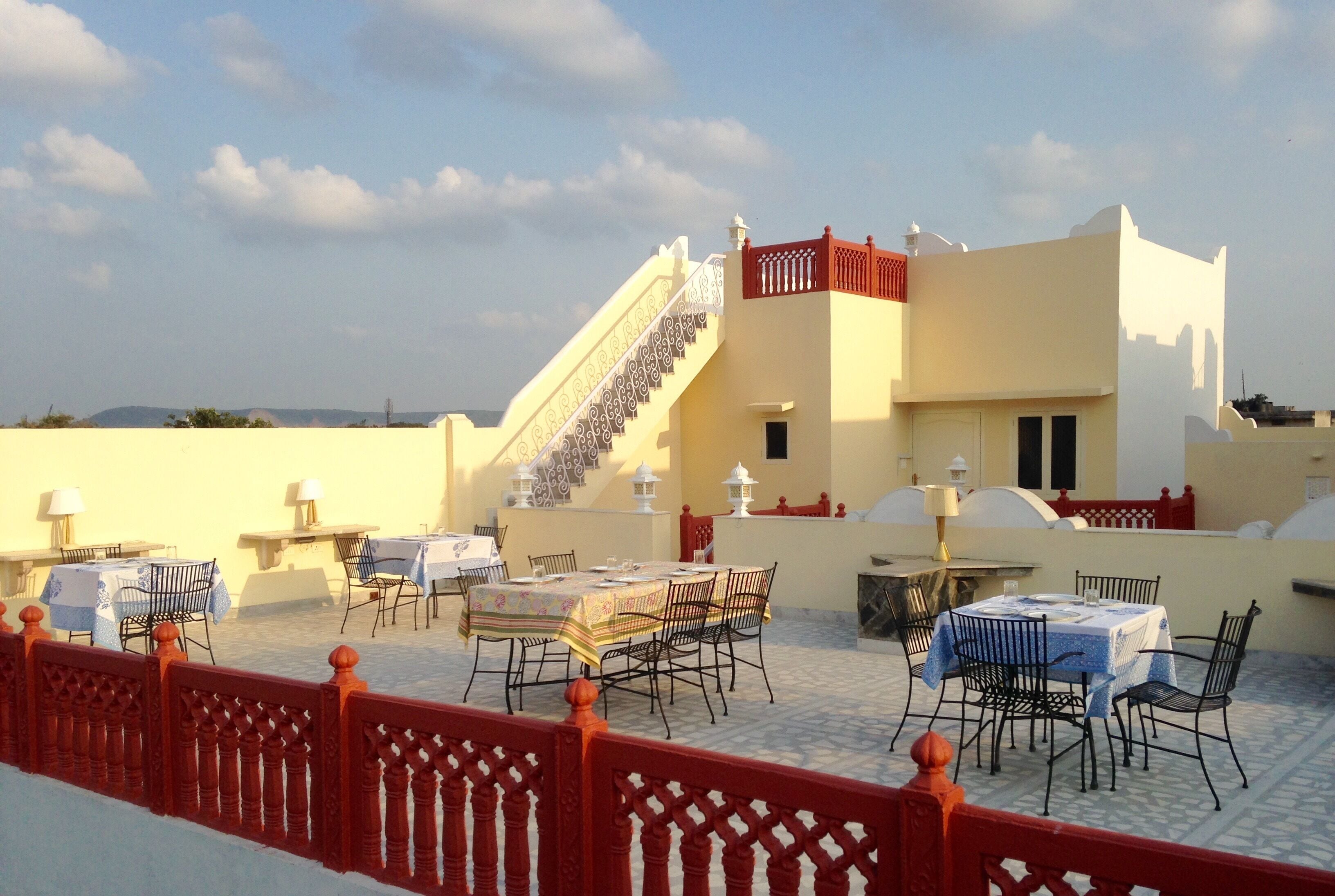 An outdoor terrace with multiple tables and chairs, a staircase, and a building with a red railing.