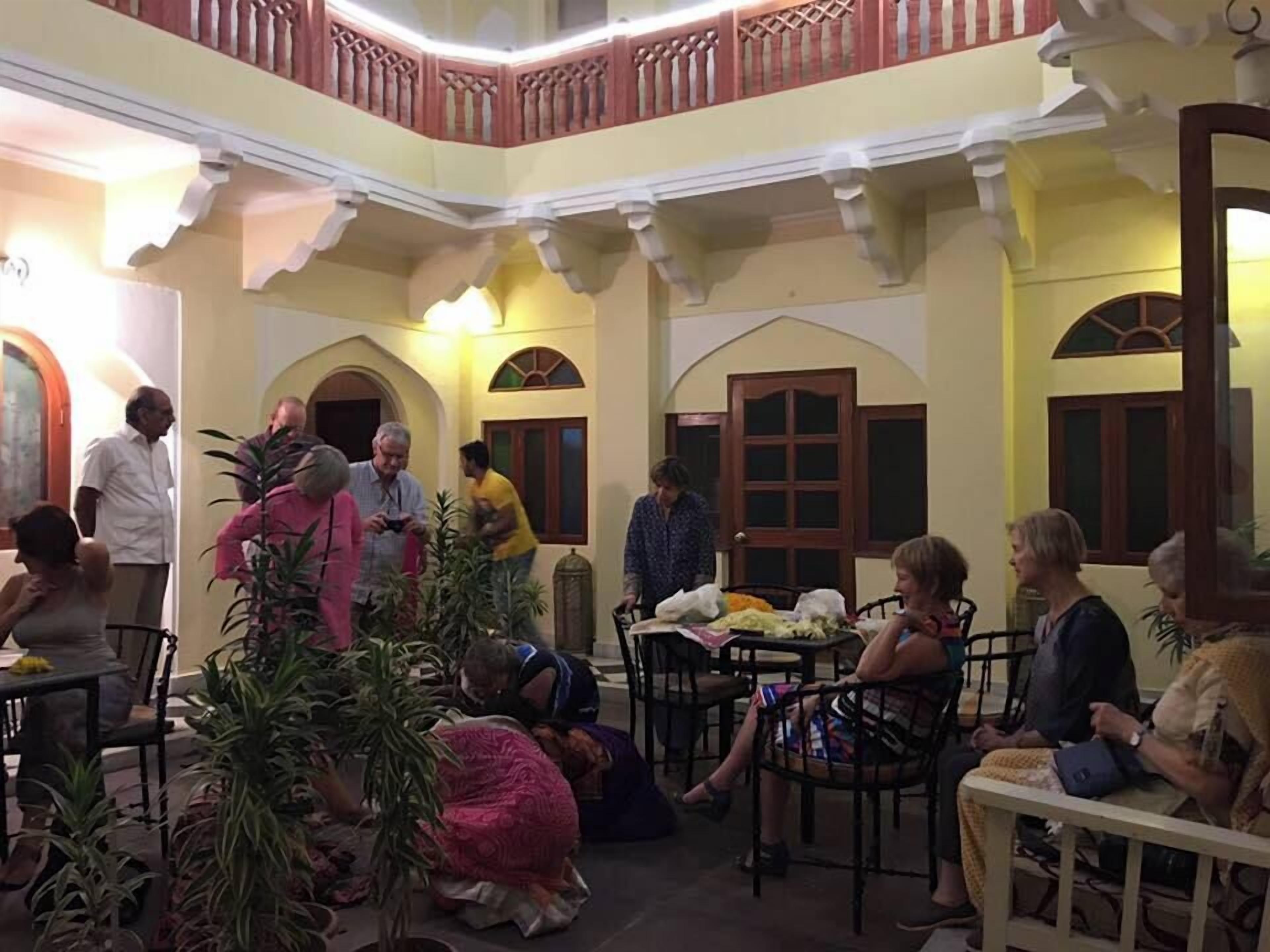 A traditional courtyard with a central seating area surrounded by arches and columns, featuring a mix of seated and standing guests.