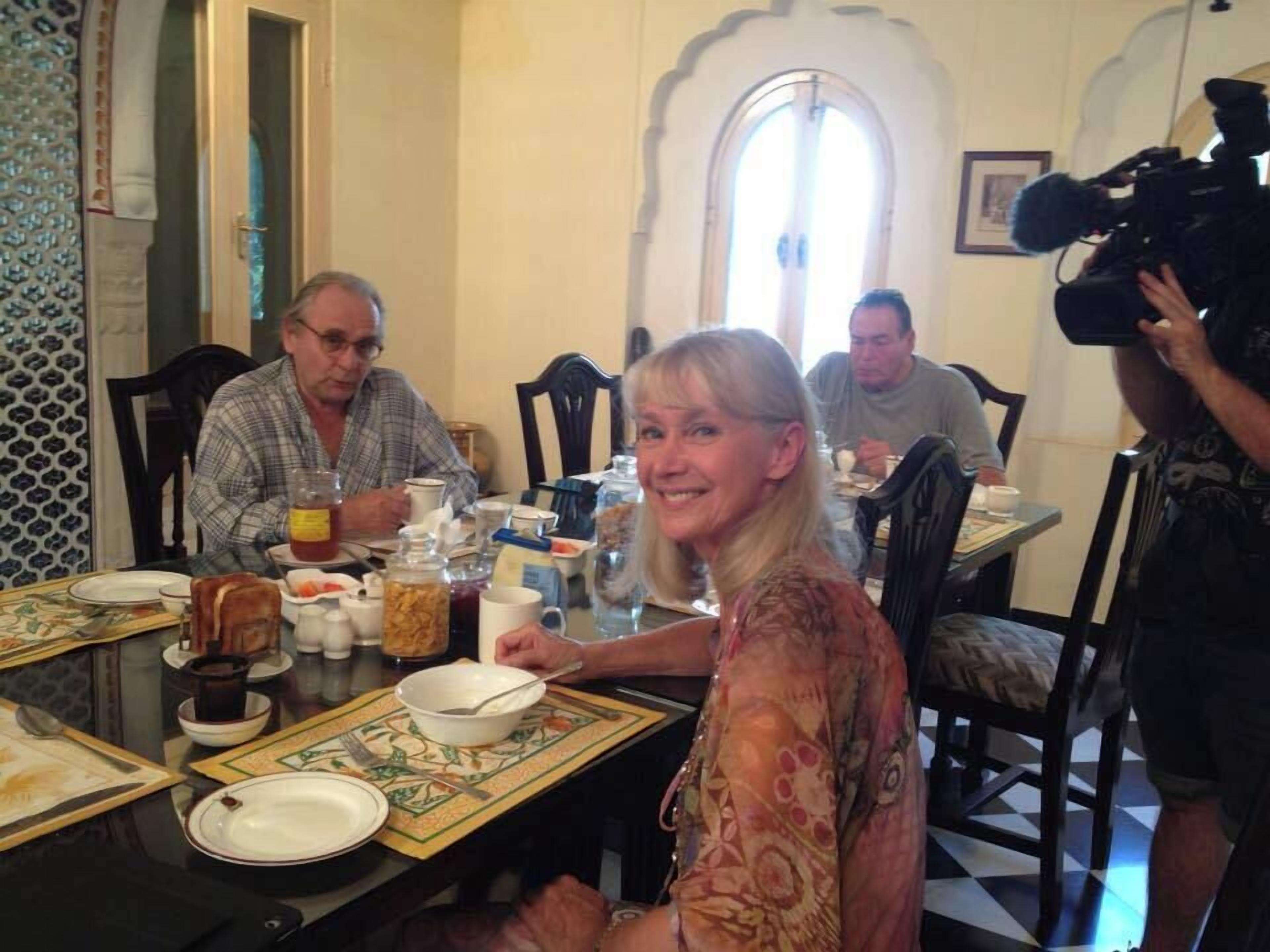 Un'area pranzo con un tavolo apparecchiato per quattro persone, una videocamera su un treppiede e una persona che sta riprendendo.