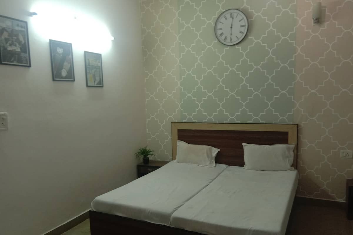 A neatly made bed with a wooden headboard, a wall clock, and framed pictures on the wall.