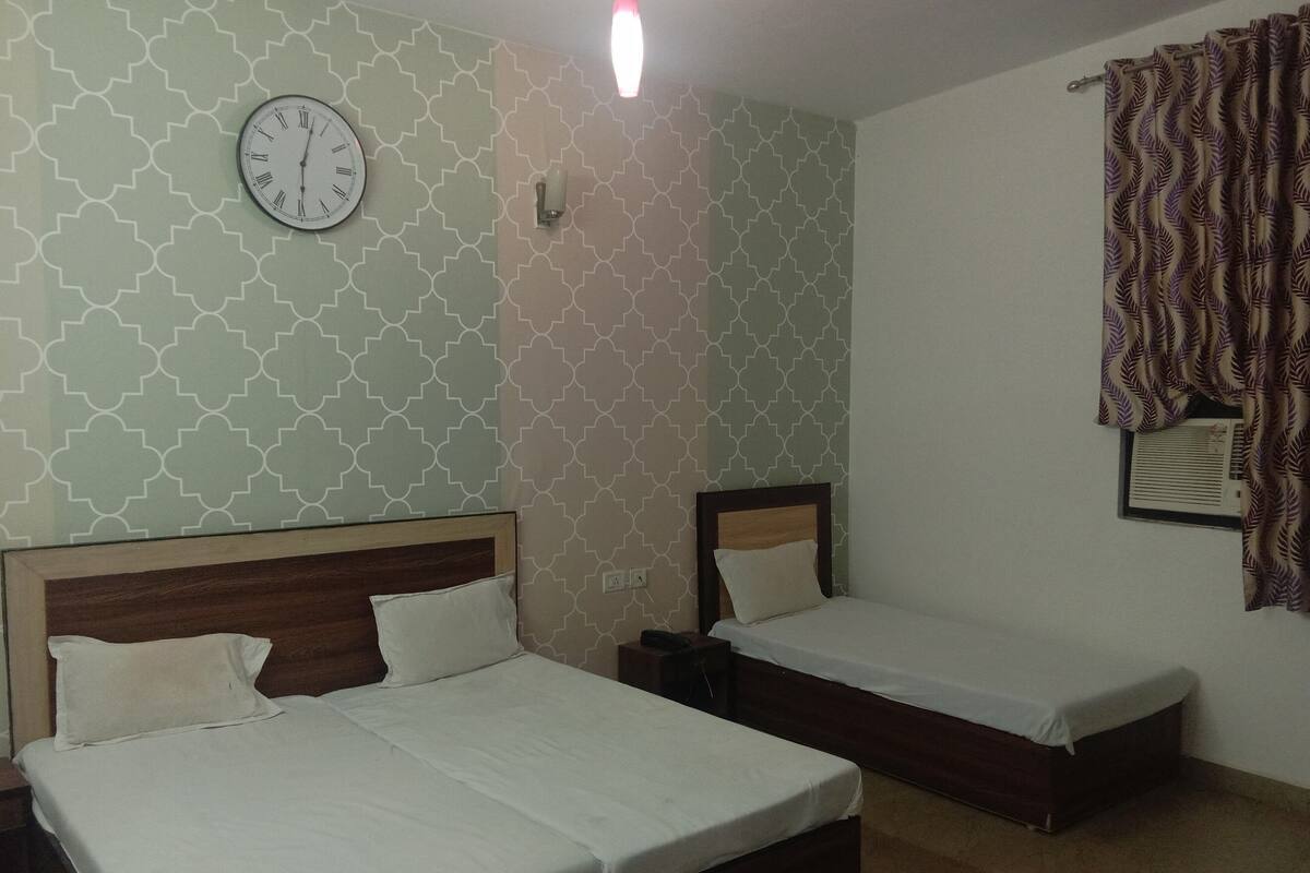 A room with two beds, a wall clock, and patterned wallpaper.