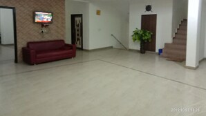 A spacious lobby with a red sofa, a television mounted on the wall, a potted plant, and a staircase. - Hotel Aicon Palace (Agra)